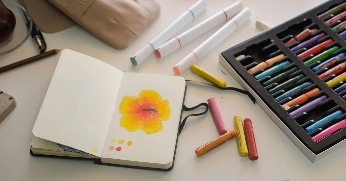 Un carnet de croquis orné d'un dessin de fleur aux couleurs éclatantes, entouré de matériel d'art coloré sur un bureau.